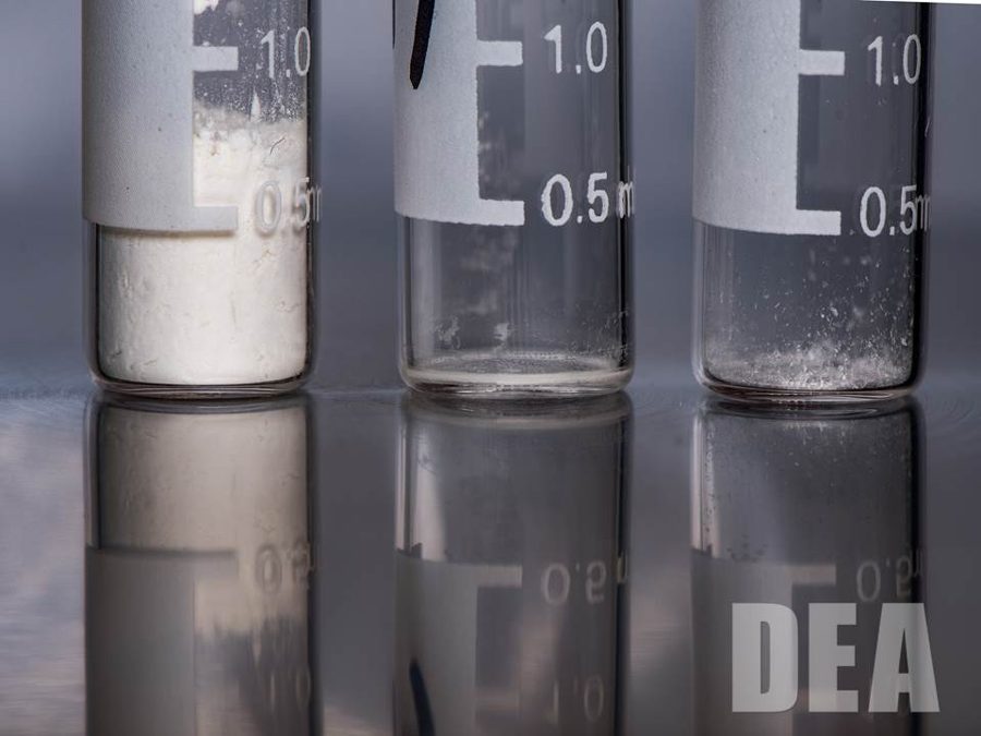 Three glass vials: a large amount of white heroin powder on the left, and tiny traces of carfentanil and fentanyl in the other two